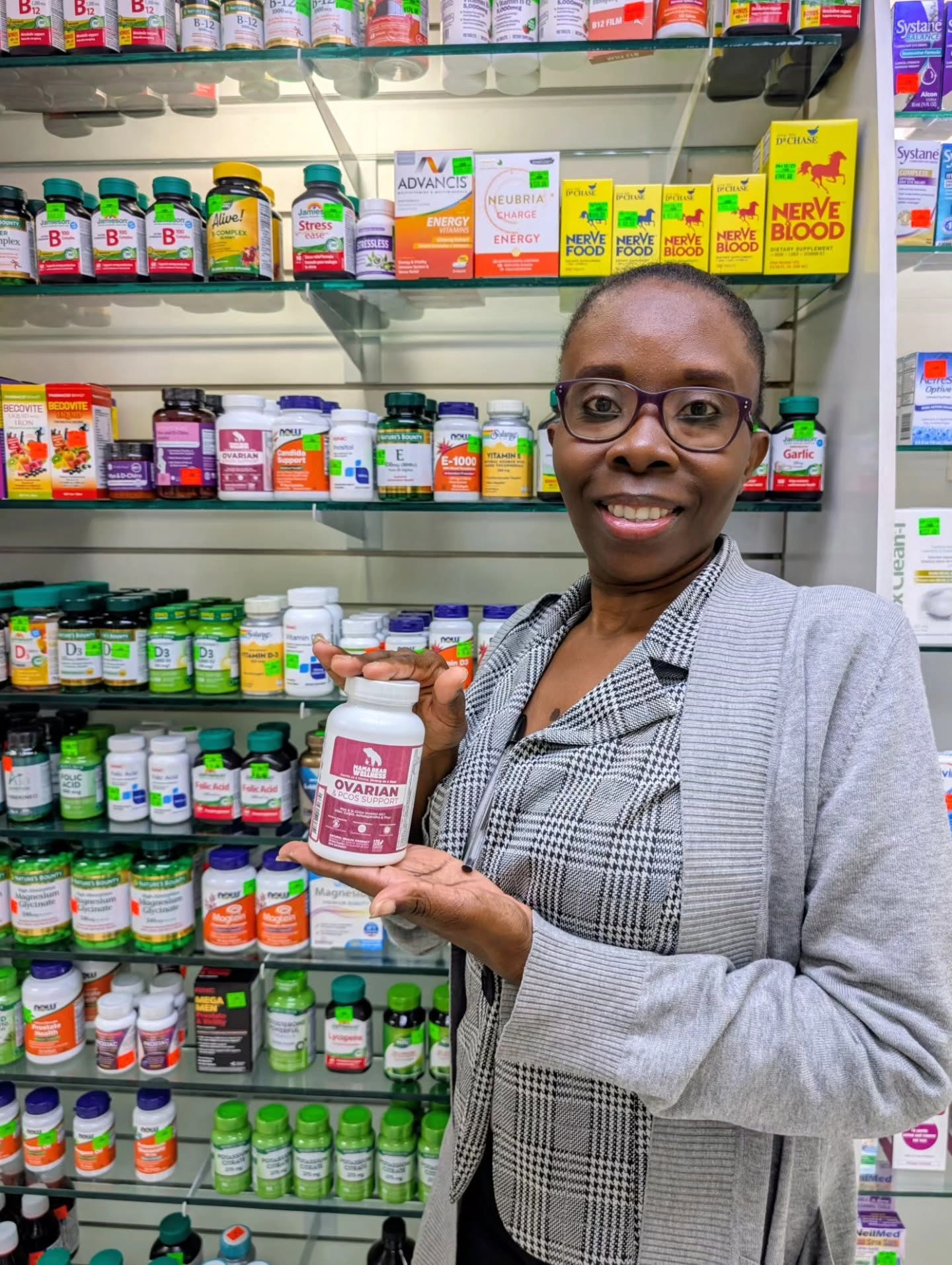 Pharmacist holding a bottle of Mama Bear Ovarian & PCOS Support beside the supplement shelves at a Trinidad pharmacy